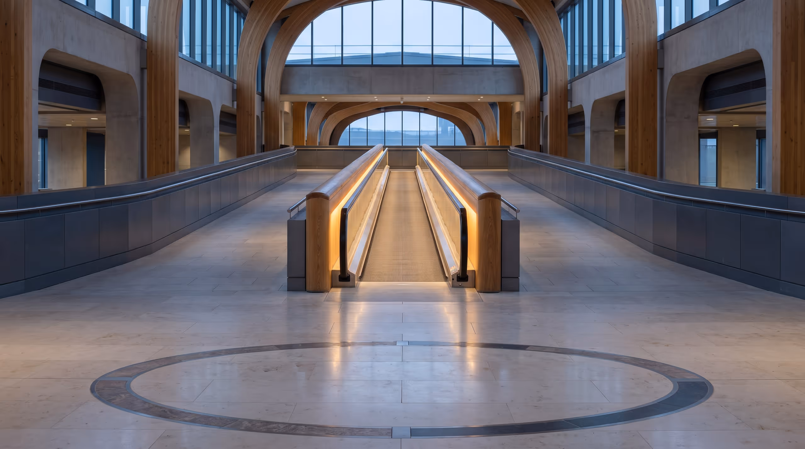 An illuminated moving walkway runs straight through an empty transit hall while broad walking routes remain open on either side.